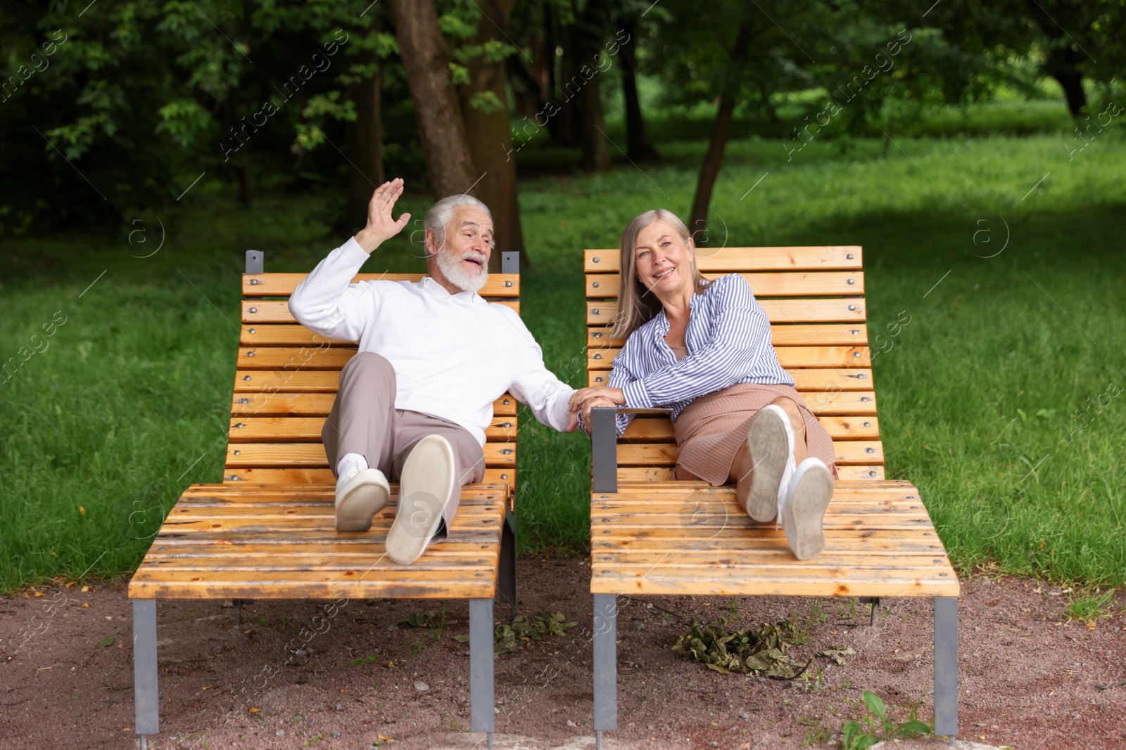 Photo of Lovely senior couple resting on wooden sunbeds in park