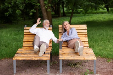 Photo of Lovely senior couple resting on wooden sunbeds in park