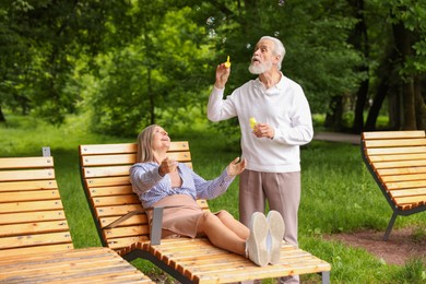 Photo of Lovely senior couple having fun with soap bubbles in park