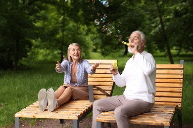 Photo of Lovely senior couple having fun with soap bubbles in park