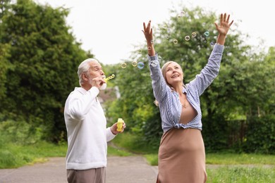 Photo of Lovely senior couple having fun with soap bubbles in park