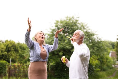 Photo of Lovely senior couple having fun with soap bubbles in park