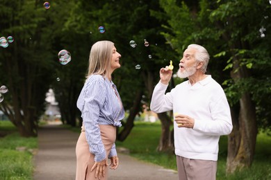 Photo of Lovely senior couple having fun with soap bubbles in park