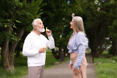 Photo of Lovely senior couple having fun with soap bubbles in park