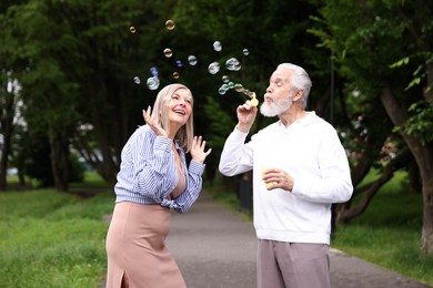 Photo of Lovely senior couple having fun with soap bubbles in park