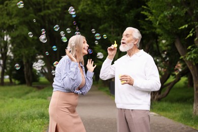 Photo of Lovely senior couple having fun with soap bubbles in park