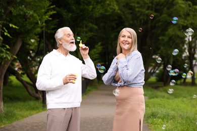 Photo of Lovely senior couple having fun with soap bubbles in park