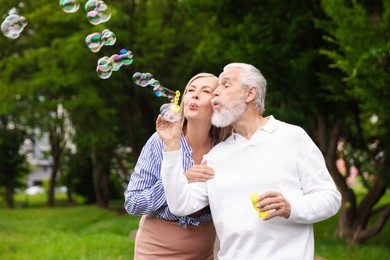 Photo of Lovely senior couple having fun with soap bubbles in park, space for text