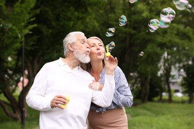 Photo of Lovely senior couple having fun with soap bubbles in park, space for text