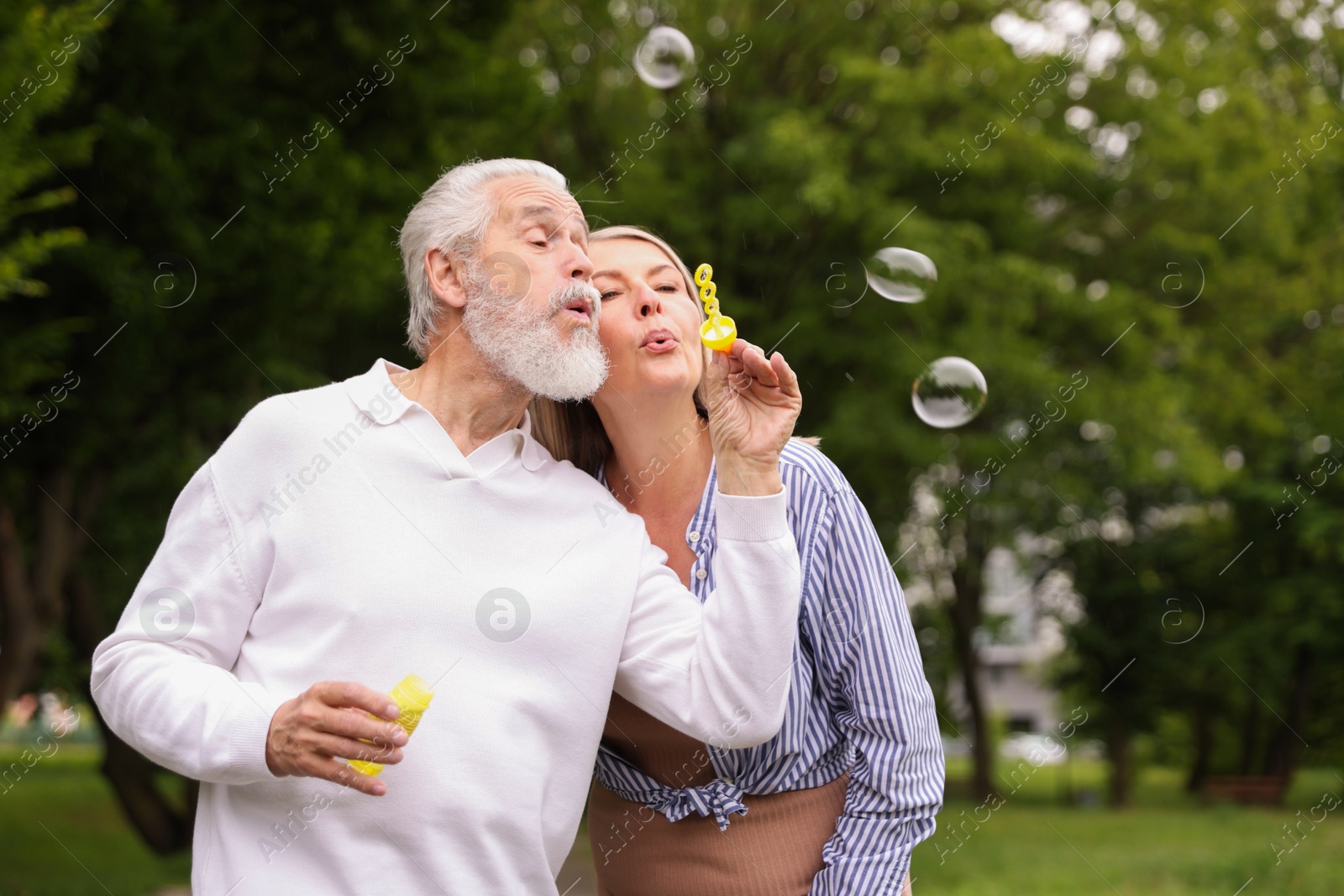Lovely senior couple having fun with soap bubbles in park, space for text Photo of Lovely senior couple having fun with soap bubbles in park, space for text