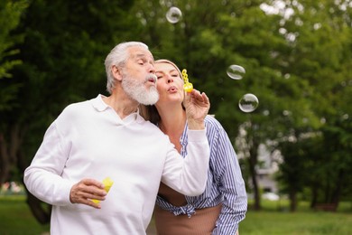 Photo of Lovely senior couple having fun with soap bubbles in park, space for text