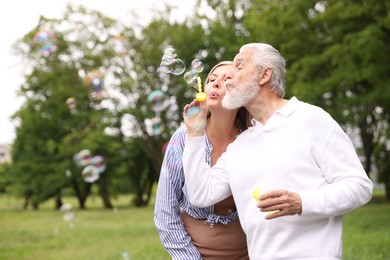 Photo of Lovely senior couple having fun with soap bubbles in park, space for text