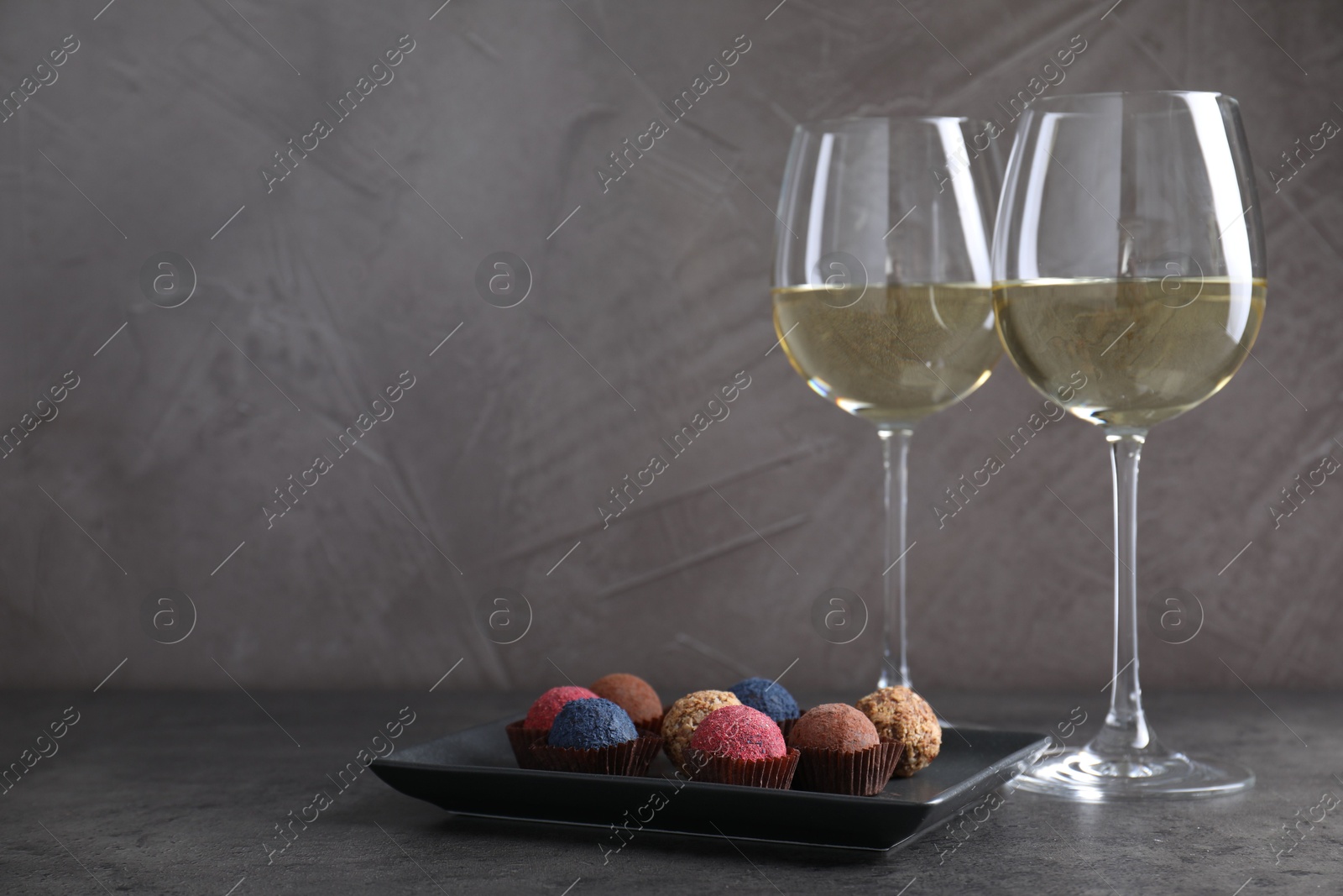 Photo of Tasty wine in glasses and truffle bonbons on grey table, space for text