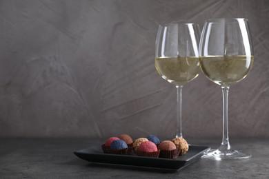 Photo of Tasty wine in glasses and truffle bonbons on grey table, space for text