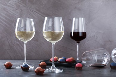 Photo of Tasty wine in glasses and truffle bonbons on grey table