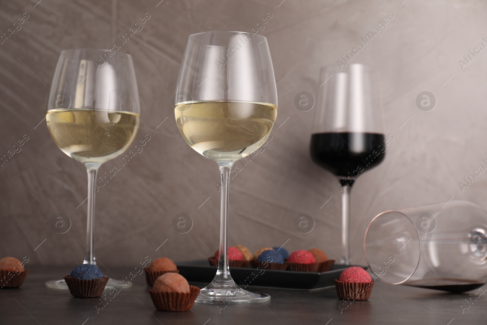Tasty wine in glasses and truffle bonbons on grey table, low angle view Photo of Tasty wine in glasses and truffle bonbons on grey table, low angle view