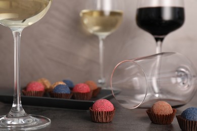 Photo of Tasty wine in glasses and truffle bonbons on grey table, closeup