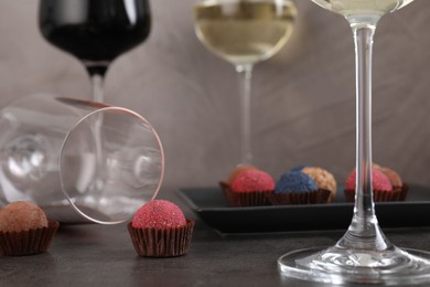 Photo of Tasty truffle bonbons and wine on grey table, closeup