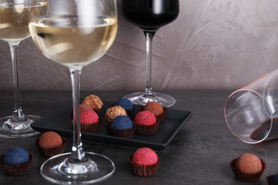 Photo of Tasty wine in glasses and truffle bonbons on grey table, closeup