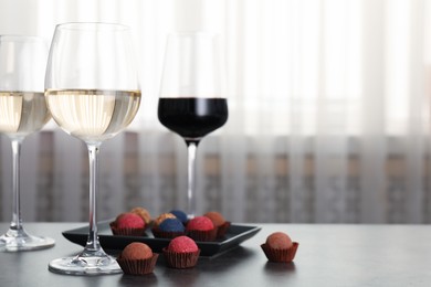 Photo of Tasty wine in glasses and truffle bonbons on grey table indoors, closeup. Space for text