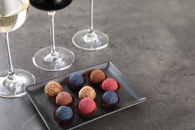 Photo of Tasty truffle bonbons and wine on grey table, above view. Space for text