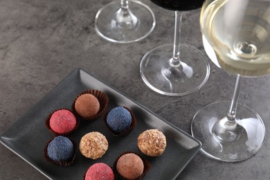 Photo of Tasty truffle bonbons and wine on grey table, above view