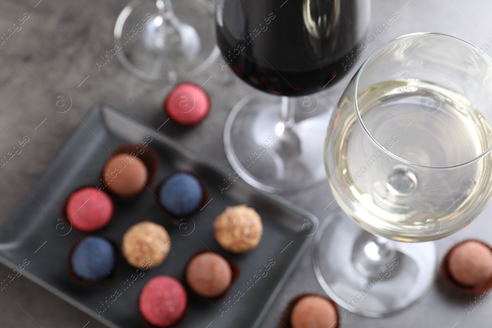 Photo of Tasty wine in glasses and truffle bonbons on grey table, above view