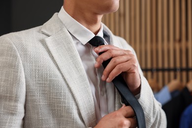 Photo of Man tying stylish necktie at home, closeup