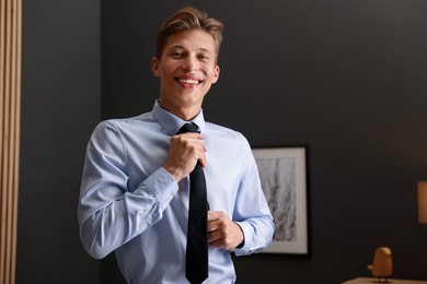 Photo of Man tying stylish black necktie at home