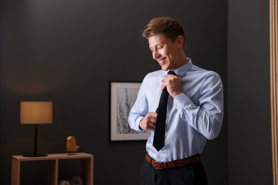 Photo of Man tying stylish black necktie at home