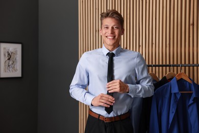 Photo of Man tying stylish black necktie at home