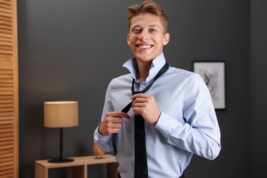 Photo of Man tying stylish black necktie at home