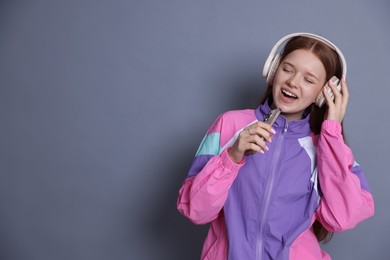 Photo of Happy teenage girl in headphones with smartphone singing on grey background. Space for text