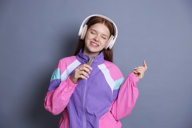 Photo of Happy teenage girl in headphones with smartphone singing on grey background