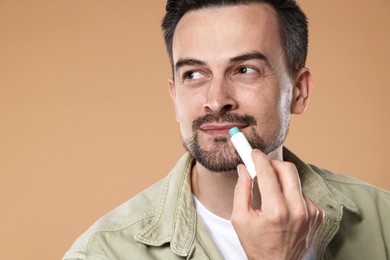 Photo of Handsome man applying lip balm onto his lips on light brown background