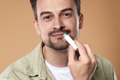 Photo of Handsome man applying lip balm onto his lips on light brown background