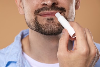 Photo of Man applying lip balm onto his lips on light brown background, closeup