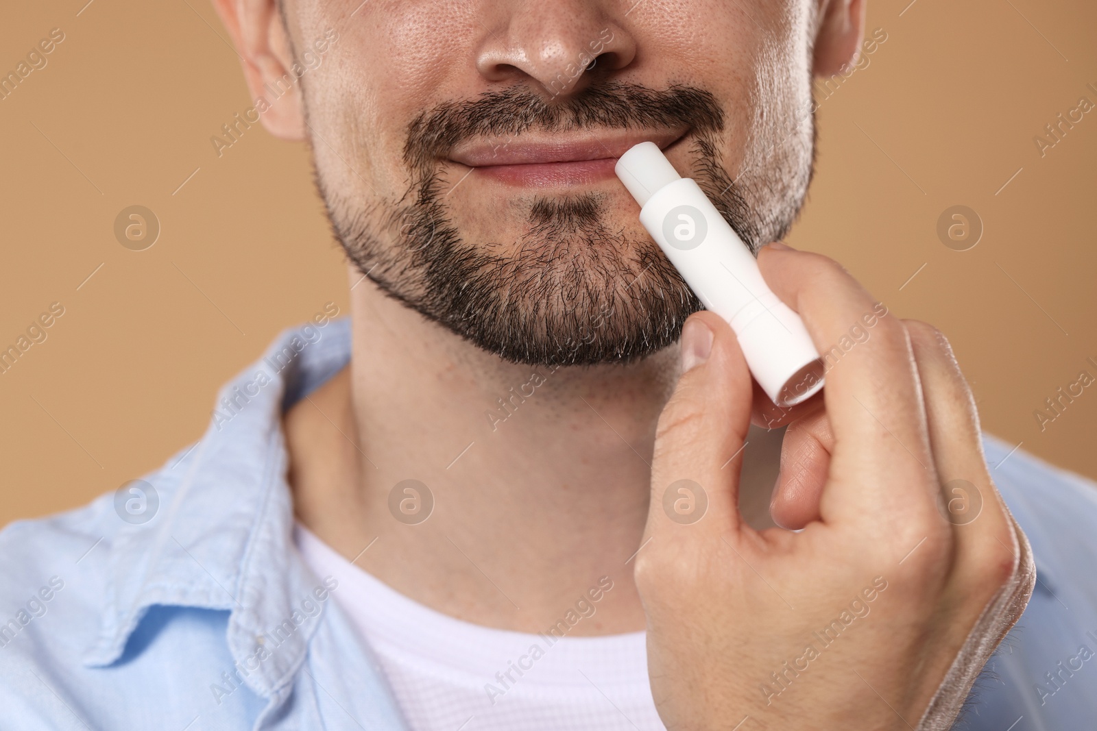 Man applying lip balm onto his lips on light brown background, closeup Photo of Man applying lip balm onto his lips on light brown background, closeup