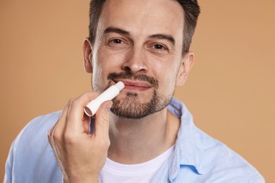 Photo of Handsome man applying lip balm onto his lips on light brown background