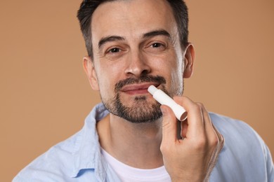 Photo of Handsome man applying lip balm onto his lips on light brown background