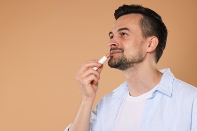 Photo of Handsome man applying lip balm onto his lips on light brown background. Space for text