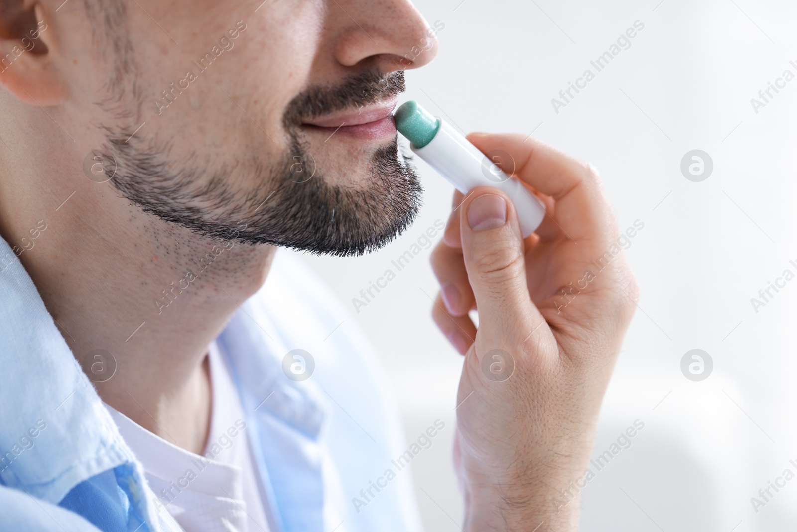 Man applying lip balm onto his lips on blurred light background, closeup Photo of Man applying lip balm onto his lips on blurred light background, closeup
