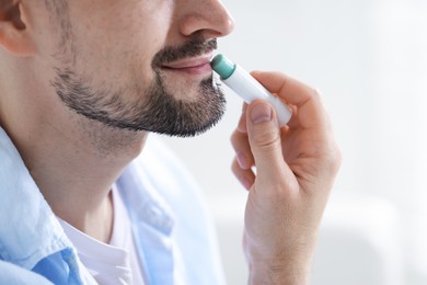 Photo of Man applying lip balm onto his lips on blurred light background, closeup