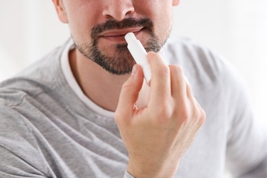 Photo of Man applying lip balm onto his lips on blurred light background, closeup