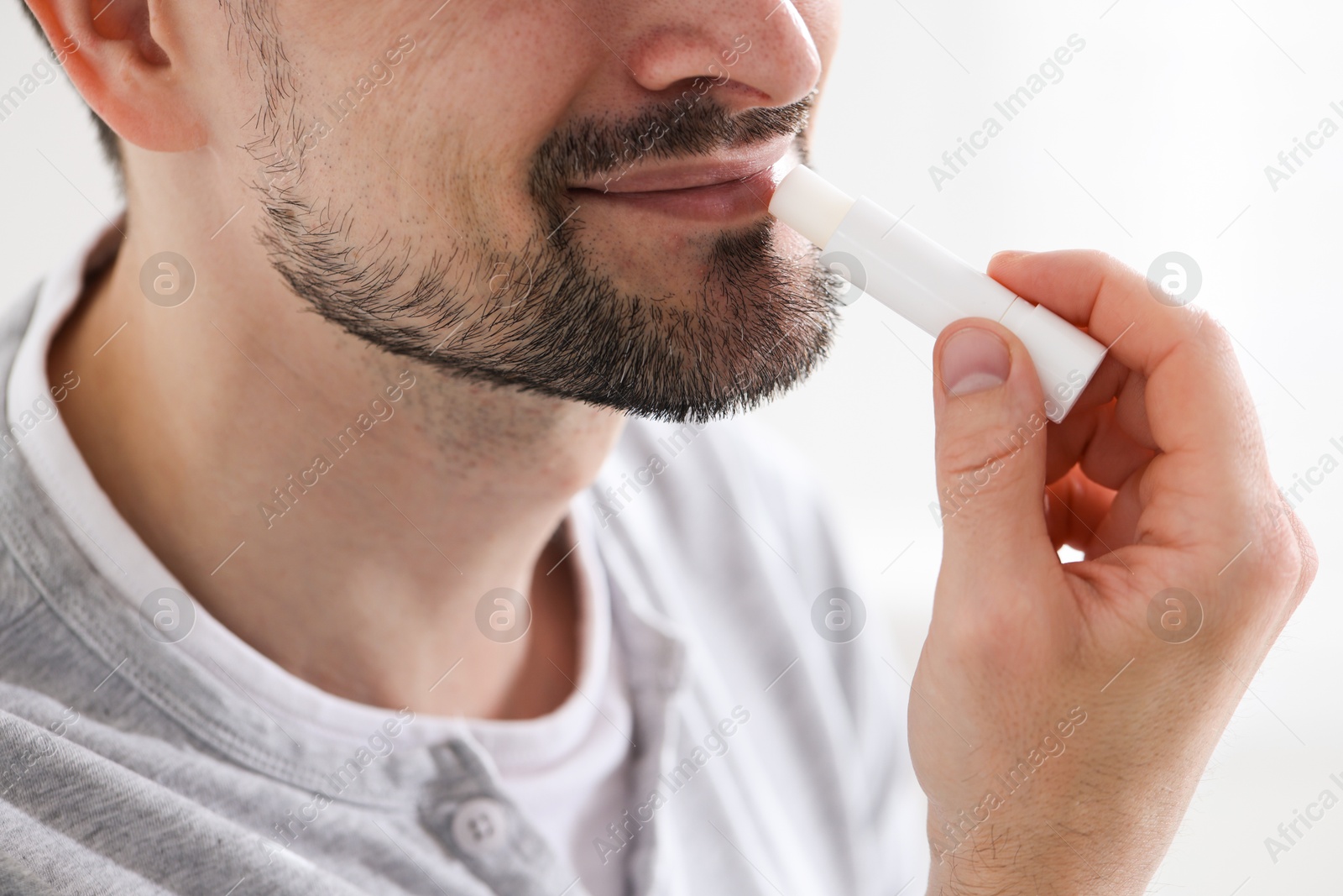 Man applying lip balm onto his lips on blurred light background, closeup Photo of Man applying lip balm onto his lips on blurred light background, closeup