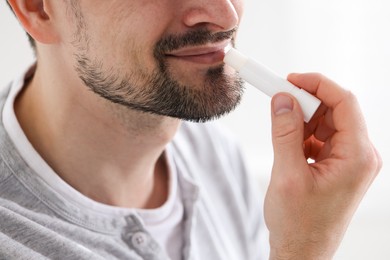 Photo of Man applying lip balm onto his lips on blurred light background, closeup