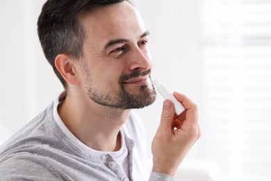 Photo of Handsome man applying lip balm onto his lips on blurred light background