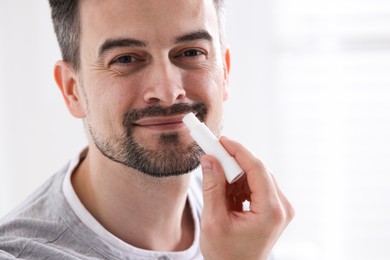 Photo of Handsome man applying lip balm onto his lips on blurred light background