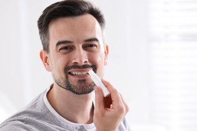 Photo of Smiling man applying lip balm onto his lips on blurred light background