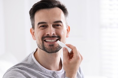 Photo of Smiling man applying lip balm onto his lips on blurred light background